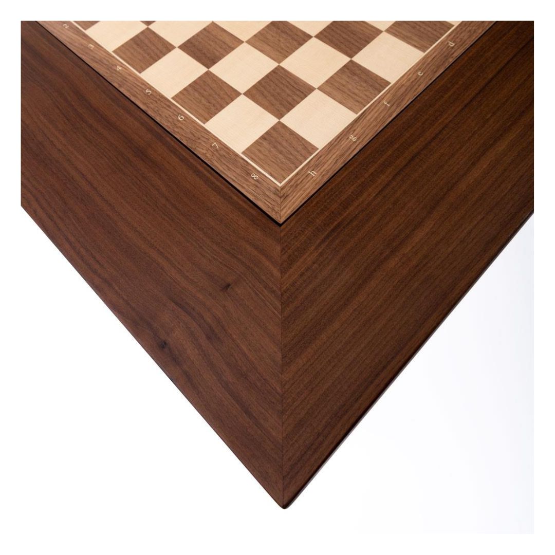 Hörnet av ett schackbord med schackbräde båda i valnöt infattade i. Bordet är något mörkare än schackbrädet