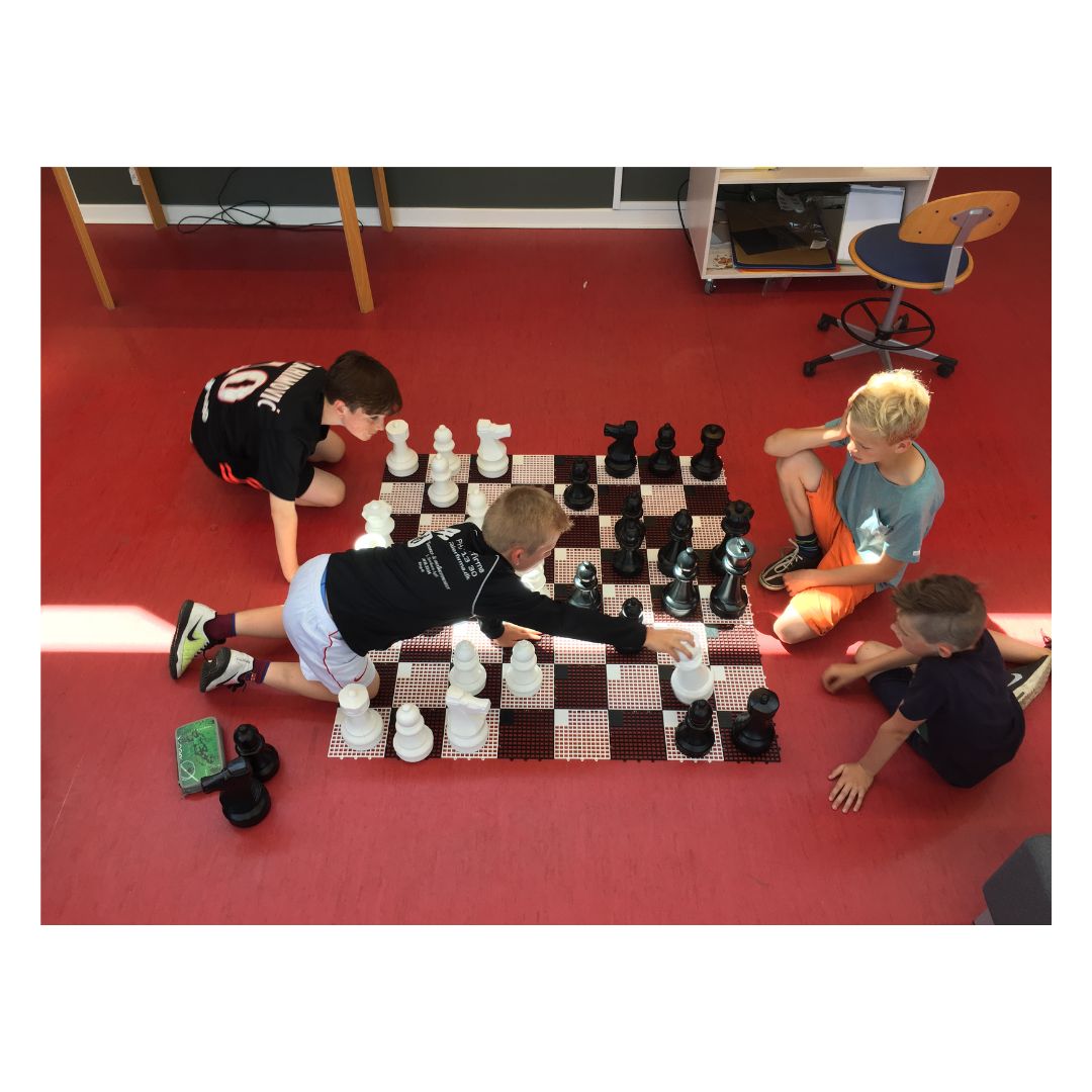 Fyra barn spelar schack i skolan med ett stort schackspel medan de funderar på sina drag