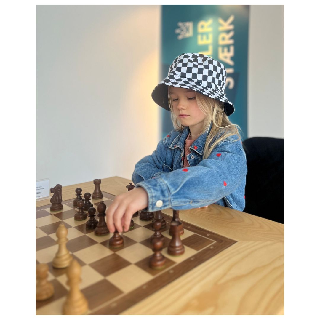 Flicka som spelar schack på ett schackbord med en schackrutig keps på huvudet i schackhuset hjärnans träningscenter