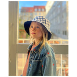 Flicka stående i ett ljust rum i schackklubbens hus, hjärnans träningscenter, med en schackrutig keps.