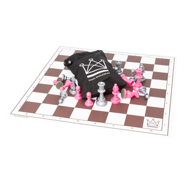 Schackspel med schackpjäser i silver och rosa tillsammans med en svart schackväska med Dansk skoleskak-logotypen tryckt på mitten av schackbrädet