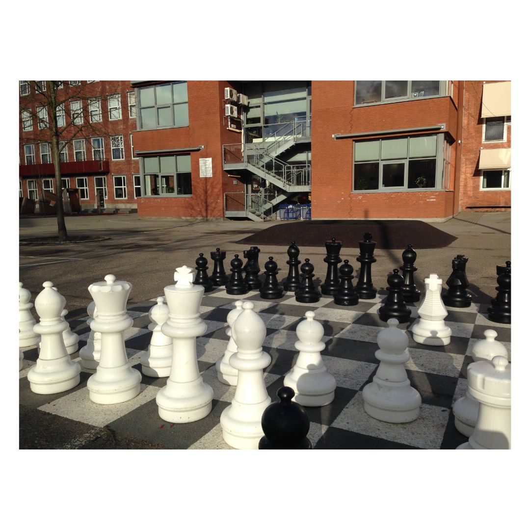 Jättelikt schackspel framför en skola i rött tegel med långa skuggor för spel sent på kvällen