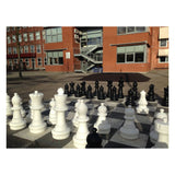 Jättelikt schackspel framför en skola i rött tegel med långa skuggor för spel sent på kvällen