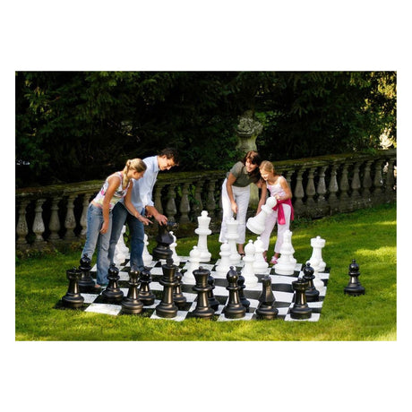 Familj som spelar jätteschack i trädgården en solig dag