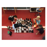 Fyra barn spelar schack i skolan med ett stort schackspel medan de funderar på sina drag