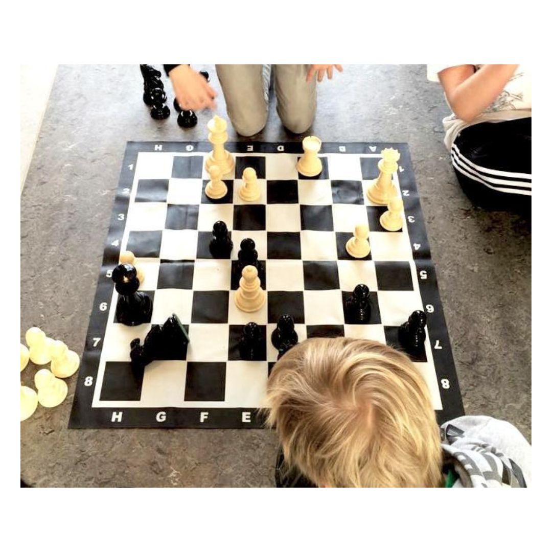 Skolbarn använder ett stort schackspel för att öva koncentration på golvet under skolans schacklektioner