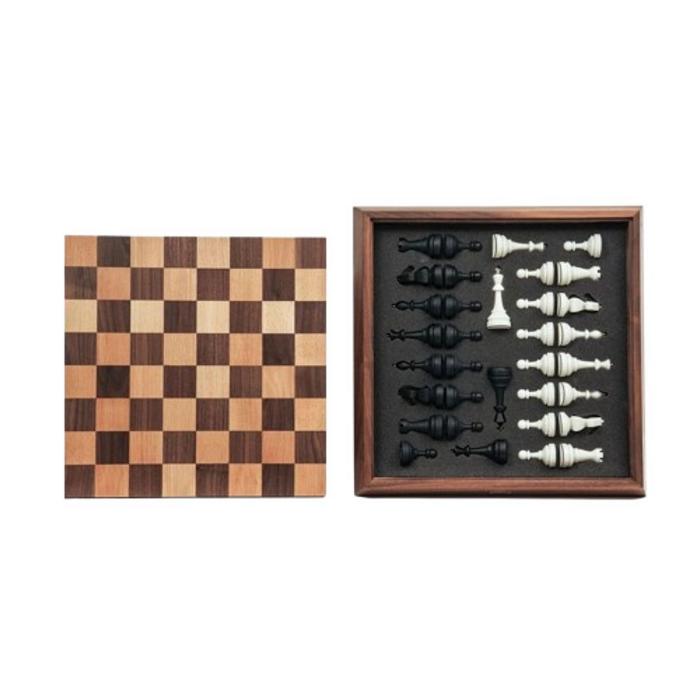 Exklusivt minimalistiskt schackset sett uppifrån. Till vänster syns schackbrädet i ljust och mörkt trä, och till höger ligger svarta och vita schackpjäser prydligt organiserade i den tillhörande förvaringslådan i trä.